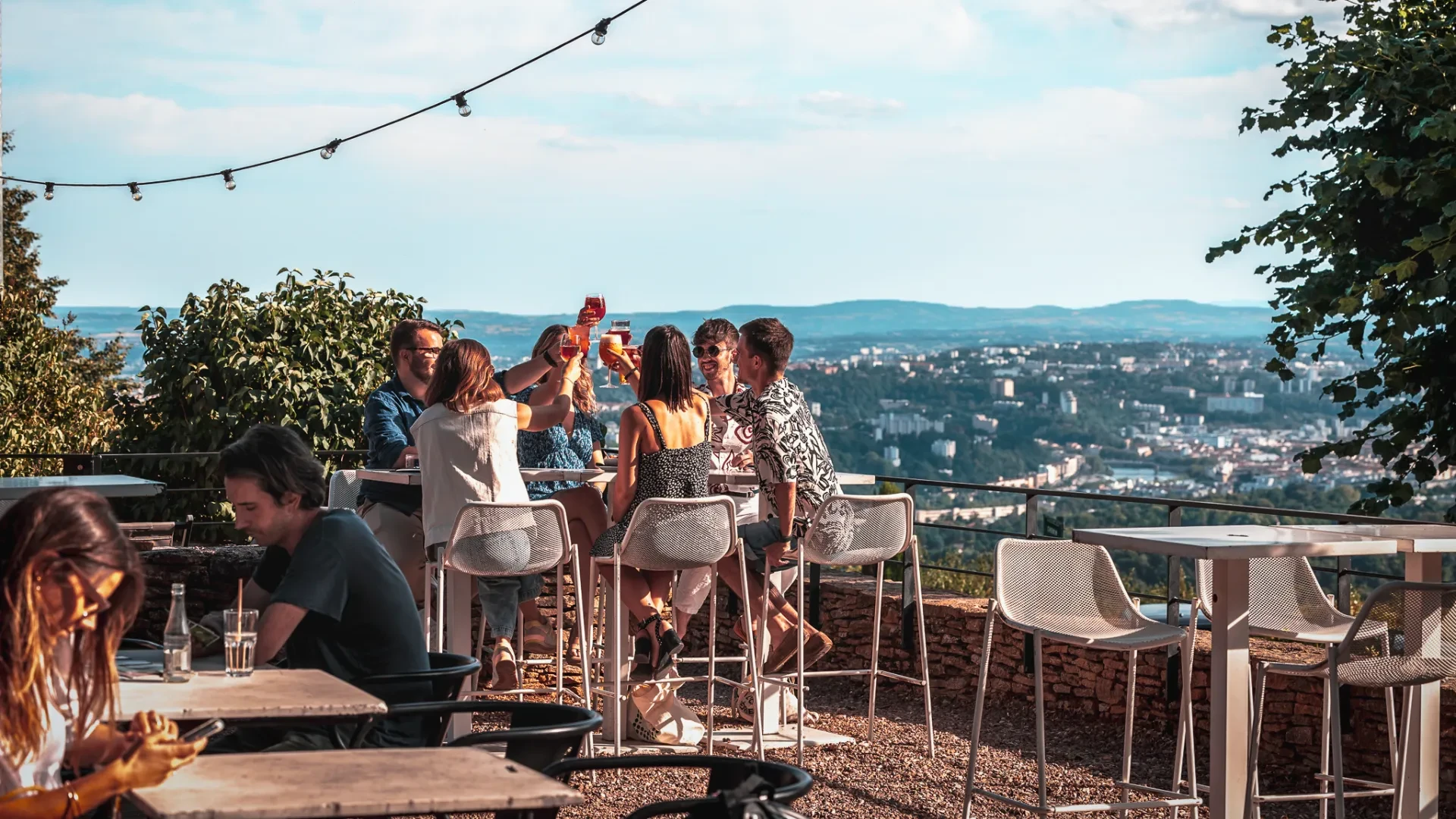 Personnes trinquent en terrasse avec vue sur la ville.